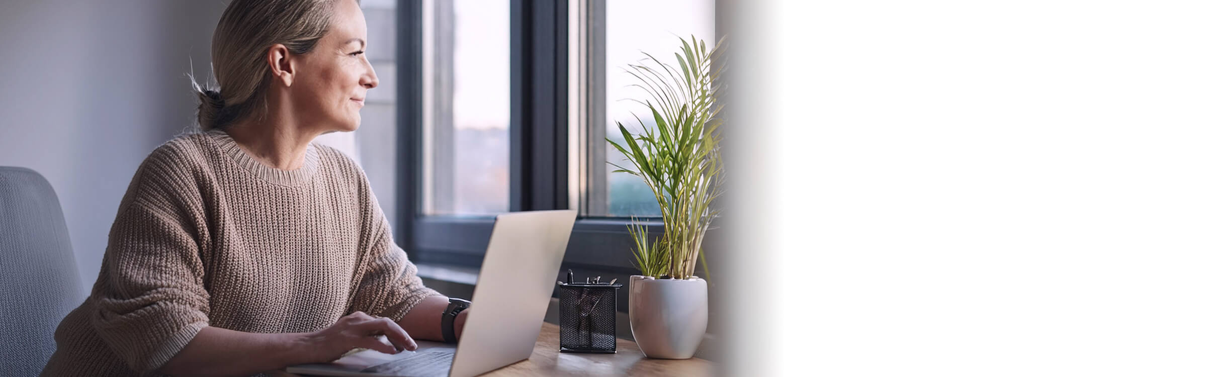 Eine Frau mittleren Alters sitzt entspannt an ihrem Arbeitsplatz.